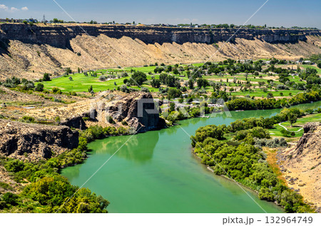 A high-angle view of the Snake River Canyon in Twin Falls, Idaho. The green river winds past a lush golf course, contrasting with the arid basalt cliffs. Represents nature, recreation, and travel 132964749