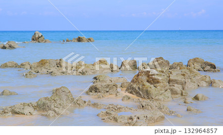 Scattered Rough Rocks Emerging from Calm Ocean Water on a Tropical Shoreline Under a Blue Sky Scattered Rough Rocks Emerging from Calm Ocean Water on a Tropical Shoreline Under a Blue Sky 132964857
