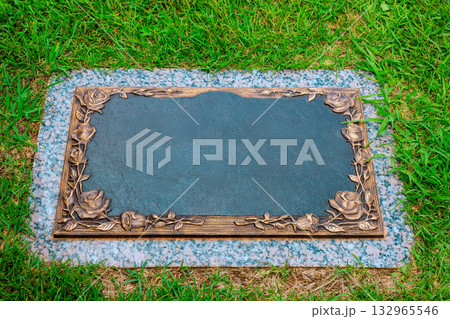 Grave marker with intricate floral details rests on lush green grass in peaceful cemetery. Grave marker with intricate floral details rests on lush green grass in peaceful cemetery. 132965546
