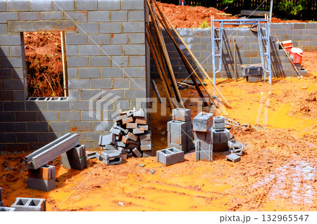Construction progress is evident with stacked blocks, tools, muddy ground at building site in residential area. Construction progress is evident with stacked blocks, tools, muddy ground at building site in residential area. 132965547