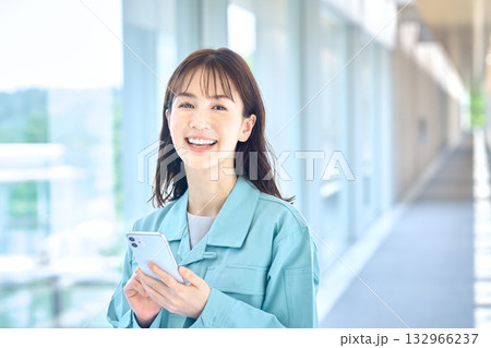 笑顔でスマートフォンを操作する作業着の女性 132966237