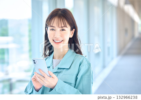 笑顔でスマートフォンを操作する作業着の女性 笑顔でスマートフォンを操作する作業着の女性 132966238