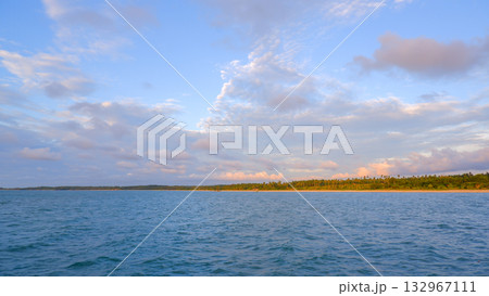 Soft Pastel Sunset/Sunrise Colors Over Ocean Water and Tropical Coastline with Palm Trees and Clouds 132967111