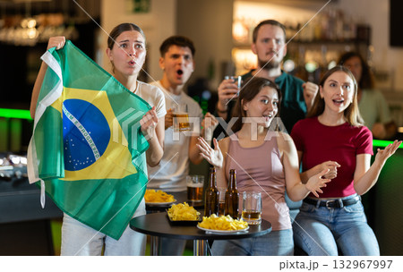 Brazilian fans with the national flag watch match on TV and express various emotions 132967997