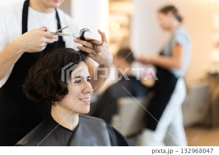 Young man barbershop employee stands next to female client, discussing details of haircut 132968047