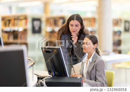 Two female students near the monitor in the library 132968058