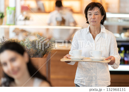 Elderly woman with coffee walking to table in cafe Elderly woman with coffee walking to table in cafe 132968131