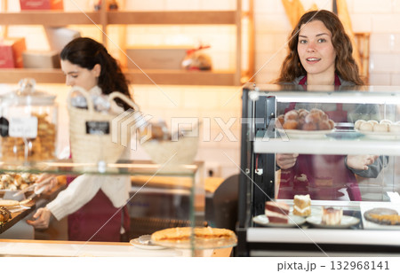 Young woman putting pastries in display case in cafe 132968141