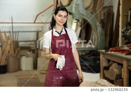 Girl employee of workshop cuts wooden board into parts using saw 132968230