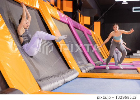 Emotive adult woman having great time while jumping on colorful trampoline in entertainment center Emotive adult woman having great time while jumping on colorful trampoline in entertainment center 132968312