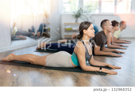 Lovers of active lifestyle on yoga mat perform doing snake cobra pose, bhujangasana in gym Lovers of active lifestyle on yoga mat perform doing snake cobra pose, bhujangasana in gym 132968352