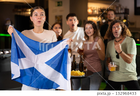 Football fans waving the flag of Scotland while drinking beer and watching tournament in sport bar 132968433