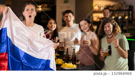 Football fans gesturing emotionally after goal scored by favorite team while watching championship match on TV in sports bar with Russian flag 132968468