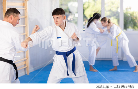 Young male attendee of karate classes fighting with middle-aged man in sports hall Young male attendee of karate classes fighting with middle-aged man in sports hall 132968469