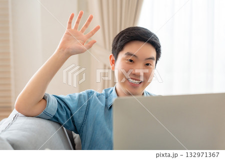 Young Asian man relaxing on comfortable couch, using laptop at home 132971367