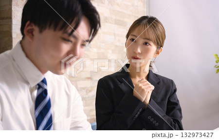 オフィスでパソコンを見ながら打ち合わせをする若い男女 オフィスでパソコンを見ながら打ち合わせをする若い男女 132973427