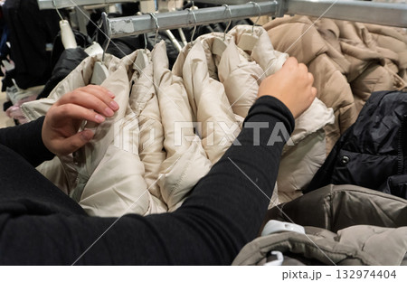 Person browsing winter jackets on clothing rack 132974404