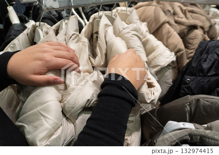 Person browsing winter jackets on clothing rack 132974415