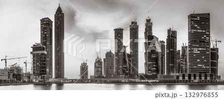 Monochrome city skyline with tall skyscrapers reflecting on calm water under a cloudy sky, Dubai Marina bay UAE Monochrome city skyline with tall skyscrapers reflecting on calm water under a cloudy sky, Dubai Marina bay UAE 132976855