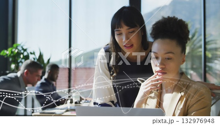 Collaborating business professionals leaning over laptop in office meeting room, with coffee mugs Collaborating business professionals leaning over laptop in office meeting room, with coffee mugs 132976948