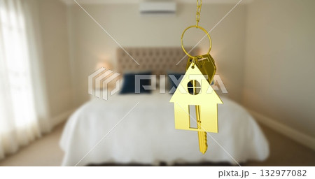 Dangling golden house-shaped keychain holding two metal keys in bedroom, with tufted headboard Dangling golden house-shaped keychain holding two metal keys in bedroom, with tufted headboard 132977082