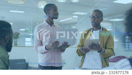 Leading meeting, two professionals holding laptop and tablet in bright office with pendant lights 132977176
