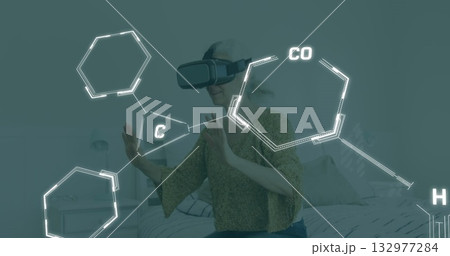 Exploring senior woman wearing virtual reality headset interacting with hexagon overlays in bedroom 132977284