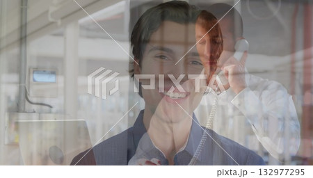 Smiling man wearing button-up shirt facing viewer in server room, with racks and telephone handset 132977295