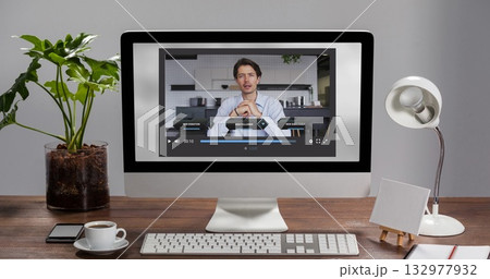 Streaming man in button-up shirt gesturing on desktop monitor at home with coffee cup, keyboard Streaming man in button-up shirt gesturing on desktop monitor at home with coffee cup, keyboard 132977932
