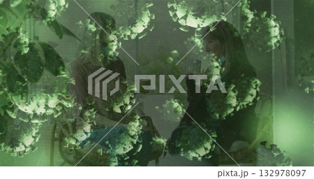 Chatting mother and adult daughter holding mugs in living room by window, with green virus overlay Chatting mother and adult daughter holding mugs in living room by window, with green virus overlay 132978097