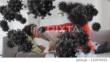 Tending mother wearing mask placing hand on resting child forehead at home, with medicine bottles Tending mother wearing mask placing hand on resting child forehead at home, with medicine bottles 132978103