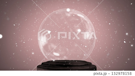 Displaying transparent glass sphere resting on dark wooden pedestal in studio, with white particles 132978158