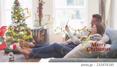 Reclining couple in sweaters taking selfie in Christmas living room, with tree, stove, copy space 132978195