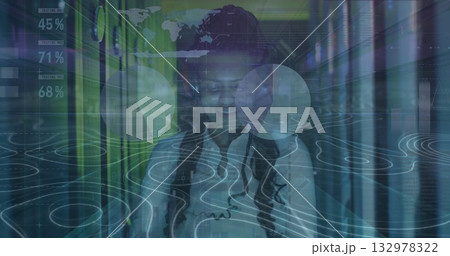 Monitoring woman IT technician in shirt checking tablet in server rack aisle, with HUD overlays 132978322