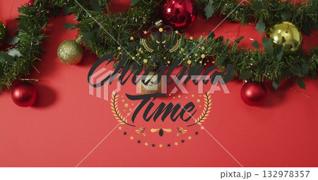 Decorating green garland lining red backdrop with red and gold baubles and Christmas Time lettering Decorating green garland lining red backdrop with red and gold baubles and Christmas Time lettering 132978357