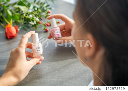A woman compares two gel nail polish bottles labeled TPO and TPO free. The concept highlights awareness of harmful ingredients like Trimethylbenzoyl Diphenylphosphine Oxide. 132978729