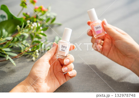 A woman compares two gel nail polish bottles labeled TPO and TPO free. The concept highlights awareness of harmful ingredients like Trimethylbenzoyl Diphenylphosphine Oxide. 132978748