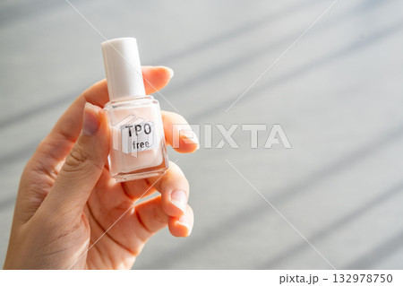 Woman holding a bottle of TPO free gel polish in bright natural light. Safe manicure product without Trimethylbenzoyl Diphenylphosphine Oxide for health-conscious consumers. Woman holding a bottle of TPO free gel polish in bright natural light. Safe manicure product without Trimethylbenzoyl Diphenylphosphine Oxide for health-conscious consumers. 132978750