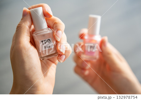 A woman compares two gel nail polish bottles labeled TPO and TPO free. The concept highlights awareness of harmful ingredients like Trimethylbenzoyl Diphenylphosphine Oxide. 132978754