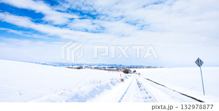 青空が覗く冬空と冬の北海道美瑛町の圧雪道路の風景 132978877