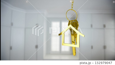 Hanging gold house-shaped keychain swinging gently in kitchen entryway, with metal keys and chain 132979047