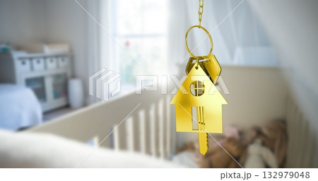 Hanging gold house-shaped keychain from short chain in softly lit nursery, with metal key near crib 132979048