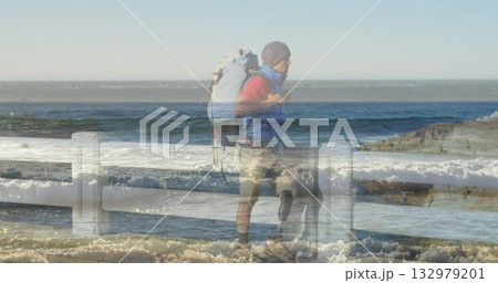 Standing hiker gazing at crashing waves behind railing coastal walkway with backpack, copy space 132979201
