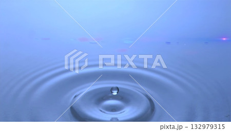 Capturing clear water droplet forming ripples on blue surface in macro setup, with lens flare 132979315