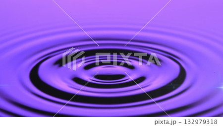 Concentric ripple rings traveling across water surface in studio basin, purple lighting 132979318