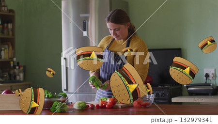 Adult woman chopping lettuce and cherry tomatoes in home kitchen, with floating hamburger cartoons 132979341