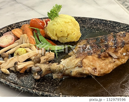 Grilled chicken steak with sauce, mushrooms and vegetables on a black plate 132979596