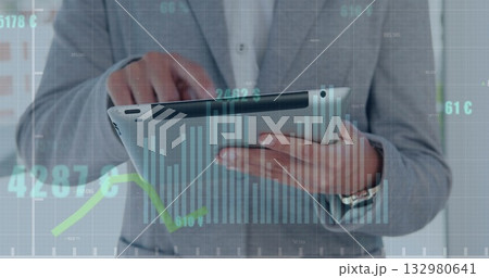 Tapping tablet businessman wearing grey suit and white shirt in office, with financial charts 132980641