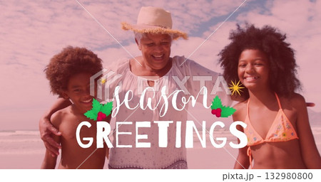 Smiling senior woman wearing straw sun hat hugging grandchildren on sandy beach, with greeting text 132980800