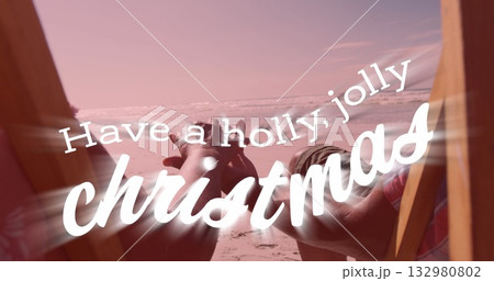 Couple in swimwear holding hands in wooden chairs on sandy shore by ocean, with Christmas overlay 132980802